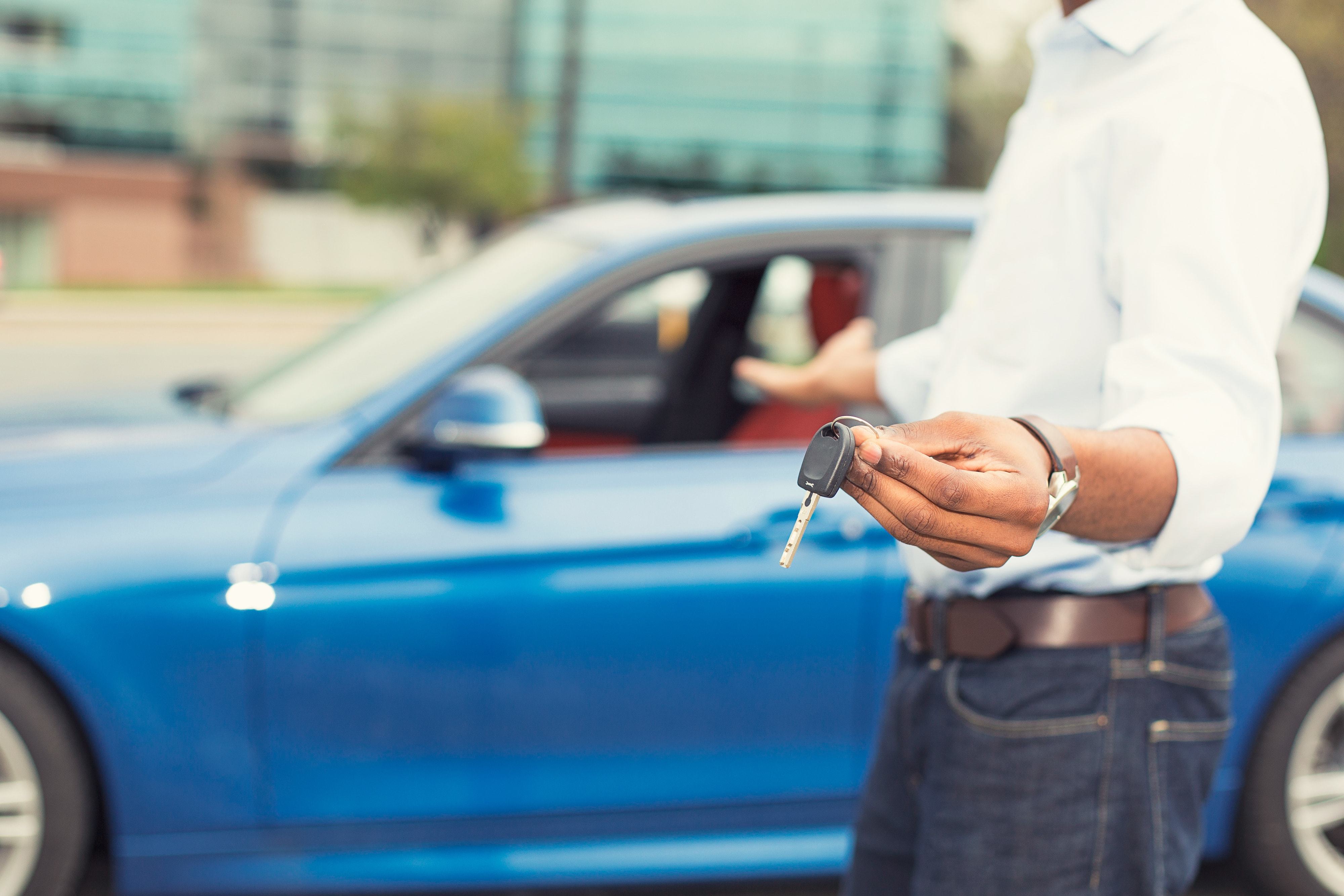 Man holding car keys in front of his newly leased car.